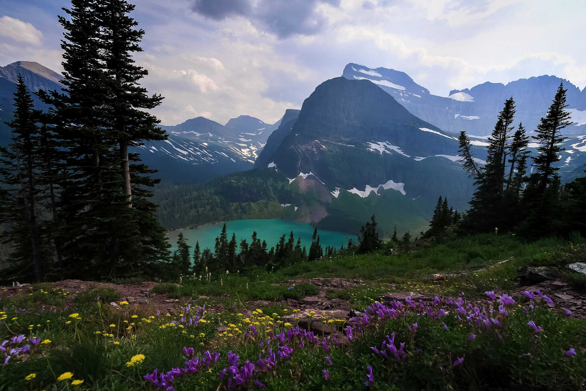 Paisaje de montaña con laguna turquesa, rodeada de pinos y flores silvestres, en un entorno natural y ecológico ideal para actividades outdoor y turismo rural.