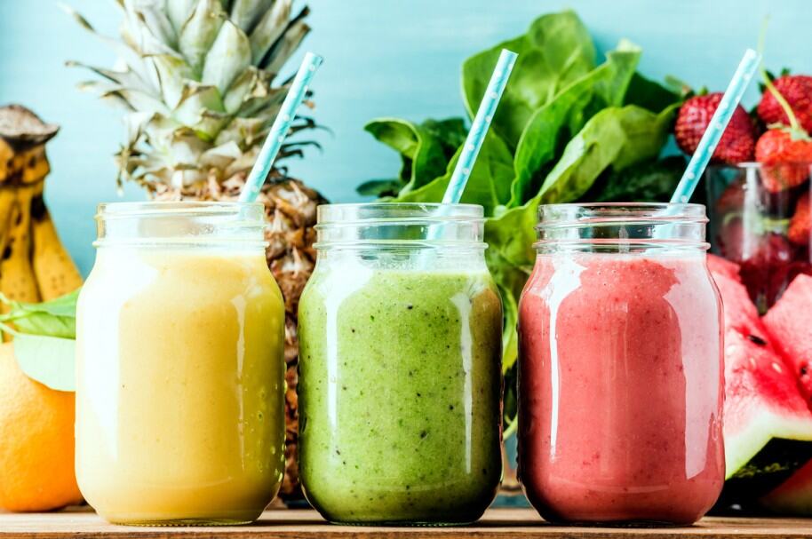 Refrescos de smoothies de frutas y verduras orgánicas en frascos, con piña, fresa y naranja en fondo de vegetales frescos.