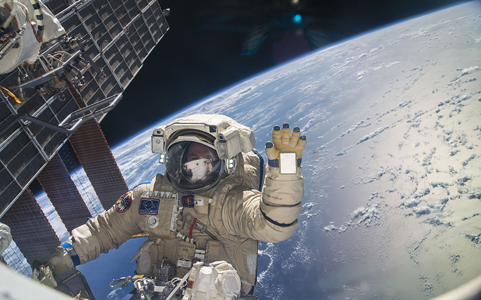 Nave espacial en órbita con astronauta saludando sobre la Tierra, imagen de alta resolución y contenido científico, ideal para temas de exploración espacial y tecnología aeroespacial.