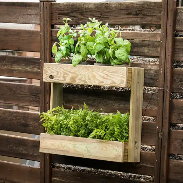 Contenedor de madera para huerto urbano con plantas de hierbas aromáticas y vegetales en macetas suspendidas en una cerca de madera. Ideal para agricultura ecológica y cultivo en espacios limitados.