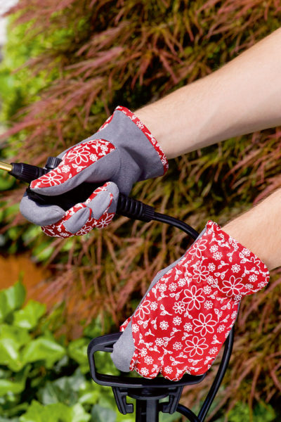 Cuidado del jardín con guantes de jardinería grises y rojos con diseño floral, manipulando un cable en un entorno natural.